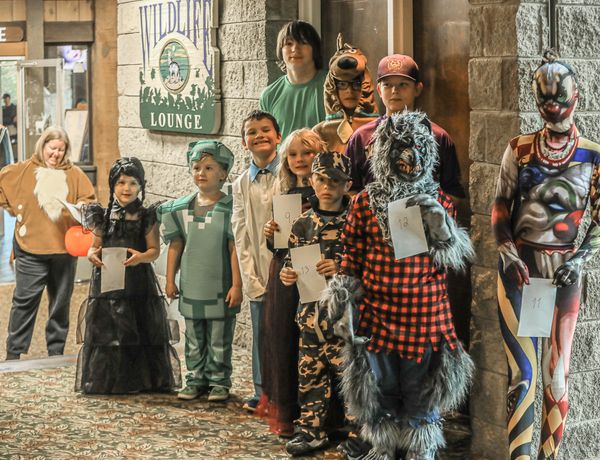 A group of children and adults dressed in Halloween costumes, including a witch, skeleton and colorful characters, pose together.
