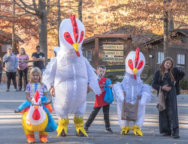 Children and adults pose with oversized white chicken characters surrounded by autumn foliage.