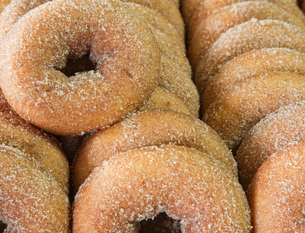 Close-up of freshly baked donuts coated in cinnamon sugar, stacked together on a tray.